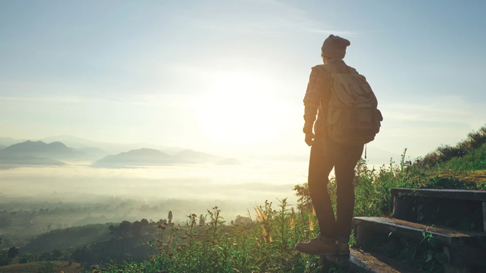 A hiker stands at the bottom of stone steps and looks westward toward a setting sun.